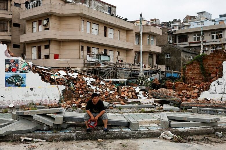 中国浙江省台州市東沙の村で、台風「バービー」の被害により崩れた壁と、そばに座る人。7月12日撮影。REUTERS/Go Nakamura