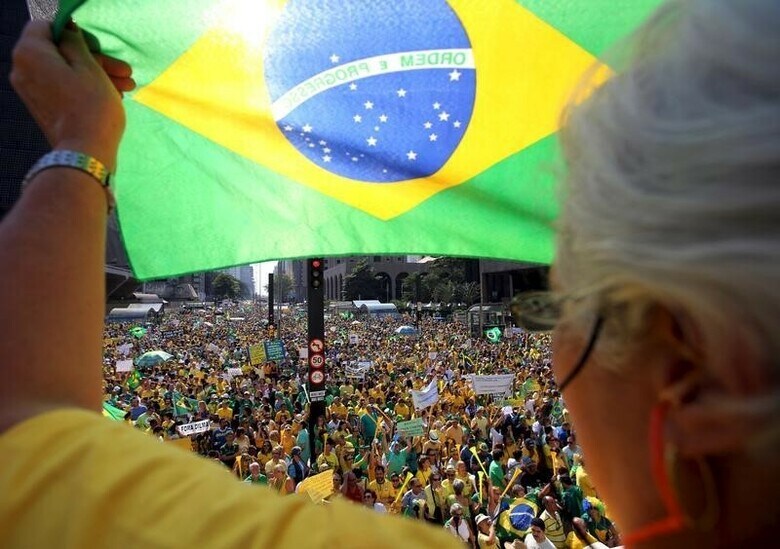 ２月２４日、格付け会社ムーディーズはブラジルの格付けをジャンク級となる「Ｂａ２」に２段階引き下げた。写真は反政府デモで国旗を掲げる参加者。昨年８月撮影。（２０１６年　ロイター／Paulo Whitaker）