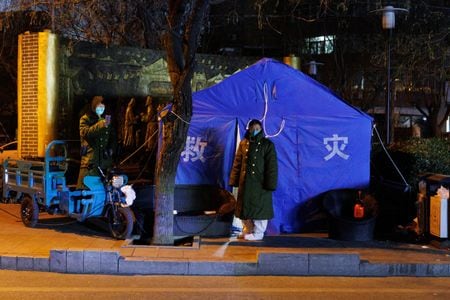 １２月４日、中国では、新型コロナウイルス対策の厳格な行動制限を緩和する動きがさらに広がった。写真は４日、北京の街頭の新型コロナ対策施設前に立つ関係者（２０２２年　ロイター/Thomas Peter）