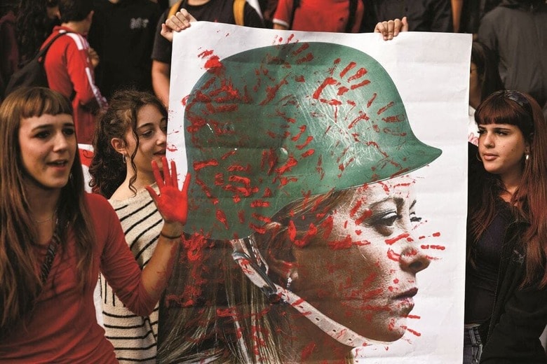 軍用ヘルメット姿のメローニのポスターに赤く塗った手形を付けるローマのデモ隊（25年11月）　MATTEO MINNELLAーREUTERS