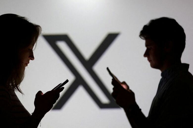 Ｘのロゴの前でスマートフォンを操作する若者のイメージ。2025年9月に撮影。REUTERS/Dado Ruvic