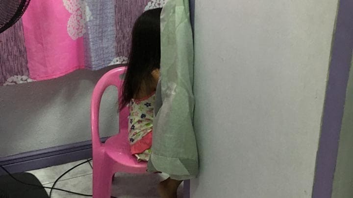 狭い診察室で母親の背中を見ている女の子（スマホ撮影）。