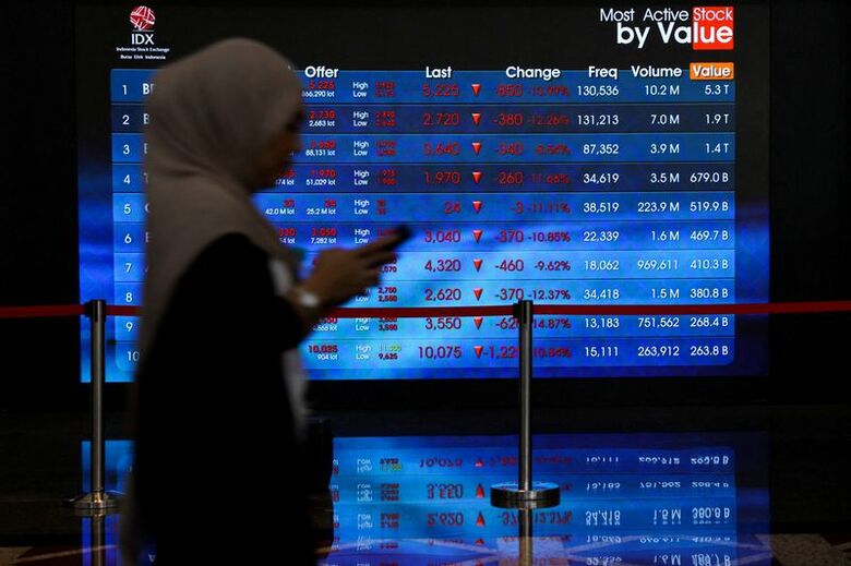 インドネシア証券取引所で、株価の動きを表示する電子掲示板の前を歩く人。10月16日、ジャカルタで撮影。REUTERS/Ajeng Dinar Ulfiana