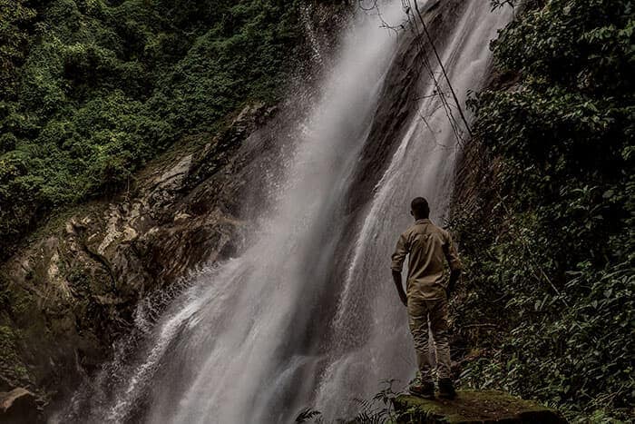 ウズングワ国立公園で最大の、高さ170メートルのサンジェ滝のそばにたたずむガイド。滝から流れる水が周辺一帯を潤し、豊かな森と生態系が維持されている