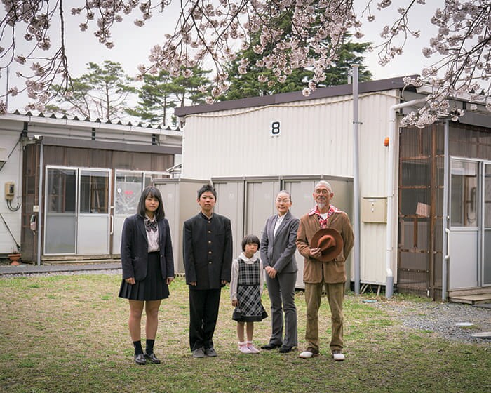 岡さん一家（2018年春）。岡さんが「忘れられない」と語る、6年7カ月に及んだ仮設住宅での暮らしを象徴する桜の下で。娘さんの入学記念の家族写真を撮影した