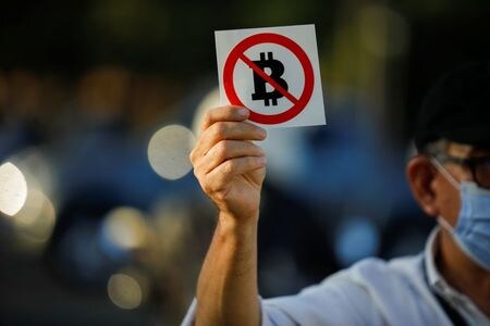 エルサドバドルでは、９月７日にビットコインが法定通貨に採用されるのを控え、広く国民全般にも不安は広がっている。写真は８月１６日、ビットコインの法定通貨化に反対するステッカーを配布する政治家のエウヘニオ・チカス氏（２０２１年　ロイター／Jose Cabezas）