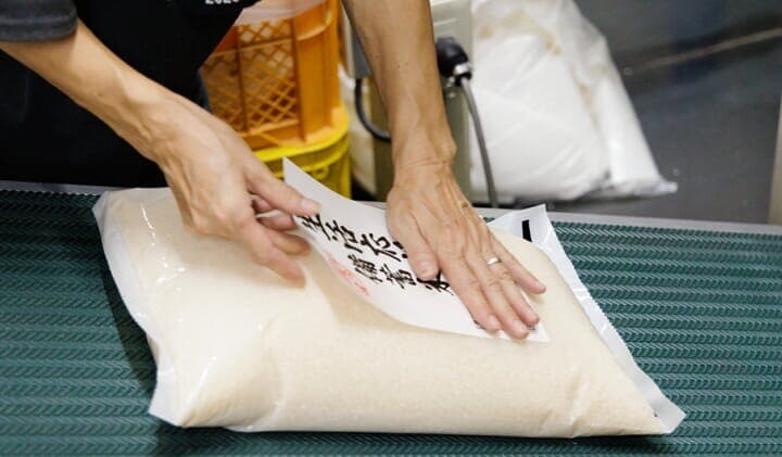 コメのパッケージにシールを貼るスタッフ