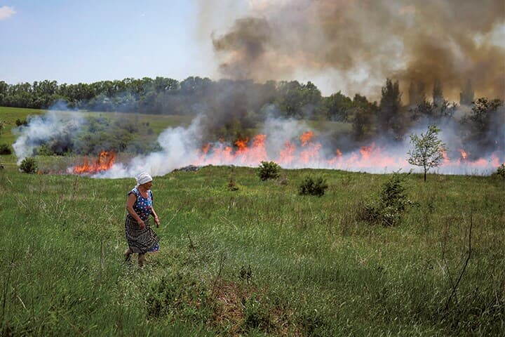 ロシア軍の激しい砲撃が続くドネツクで、炎上する畑を横目に去る女性　GLEB GARANICHｰREUTERS