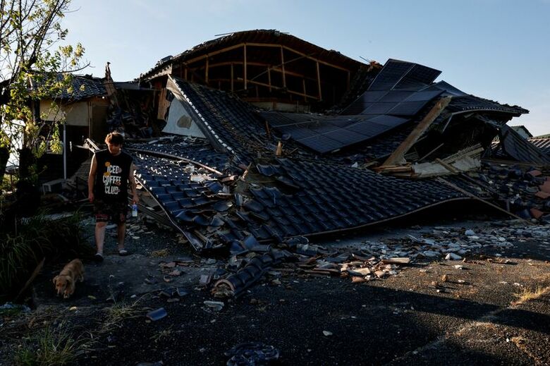 地震によって倒壊した、熊本県八代市氷川町の住宅と、その周辺で愛犬を散歩させる男性。7月31日撮影。REUTERS/Kim Kyung-Hoon