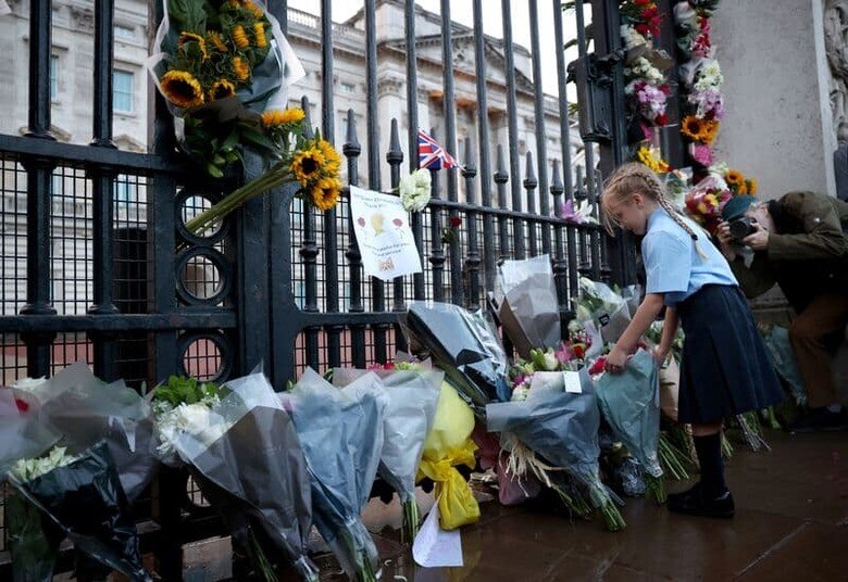 「英国の顔」として70年以上にわたって親しまれてきたエリザベス女王の訃報を受け、世界各地では要人だけでなく、多くの市民らも哀悼の意をささげた。写真はバッキンガム宮殿の門の前で献花する少女（2022年　ロイター／Henry Nicholls）