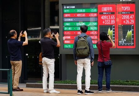 　７月８日、日本企業の今３月期第１四半期決算シーズンが７月後半に始まる。写真は４日、都内の株価ボード前で写真を撮る人々（２０２４年　ロイター/Kim Kyung-Hoon）