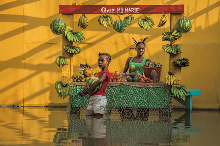 ボードワン・ムワンダ(Baudouin Mouanda)<br>
<シリーズタイトル> 『ある季節の空』<br>
(Ciel de saison / Seasonal Sky)<br>
<作品タイトル> 野菜売りの店で(2020年)<br>
(Chez la marchande de légumes)<br>
▶コロナ禍にあった2020年にコンゴ共和国の首都ブラザビルで起きた洪水を、被災者たちの協力で再現した。現地では雨の脅威が恒常的なものになっている<br>
Credit: Courtesy Baudouin Mouanda