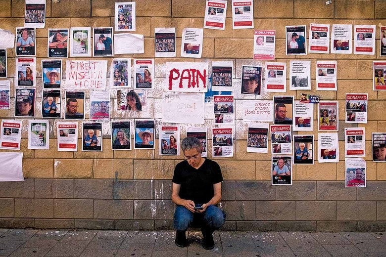 ハマスに拉致された人々のポスターが並ぶ壁の前で座り込むイスラエル市民　AMIR LEVY/GETTY IMAGES