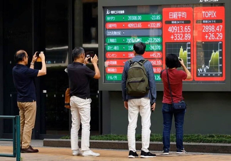 ７月８日、日本企業の今３月期第１四半期決算シーズンが７月後半に始まる。写真は４日、都内の株価ボード前で写真を撮る人々（２０２４年　ロイター/Kim Kyung-Hoon）