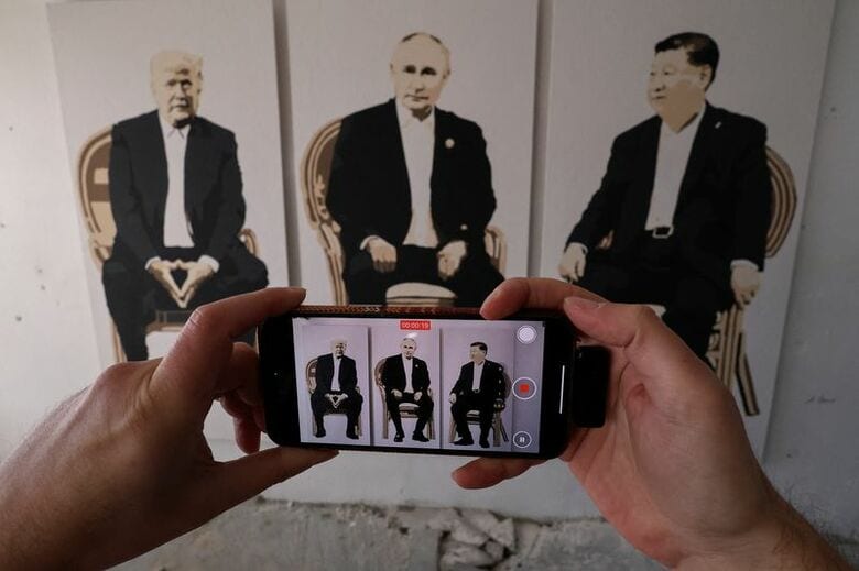 写真はクリミアのヤルタで開かれた展覧会に展示された、トランプ米大統領、ロシアのプーチン大統領、中国の習近平国家主席を描いた作品と、作品を撮影する人の手。2025年2月撮影。REUTERS/Alexey Pavlishak