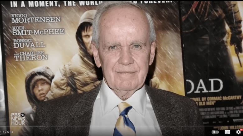 生涯を通じて、暗く暴力的な世界と格闘し続けた作家、コーマック・マッカーシー（後ろは映画化された『ザ・ロード』のポスター　PBS/YouTube