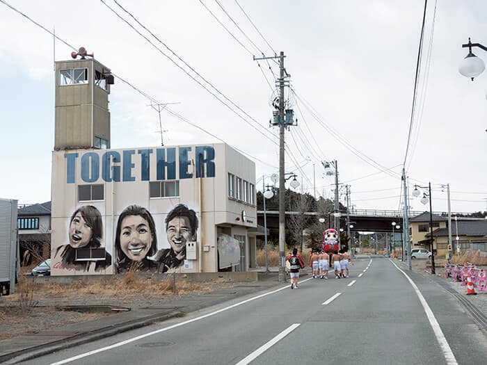 新春恒例「双葉町ダルマ市」の神輿巡幸（双葉町、26年）。避難先のいわき市で継続され、23年に町内で復活。かつてにぎわった商店街の建物は激減した