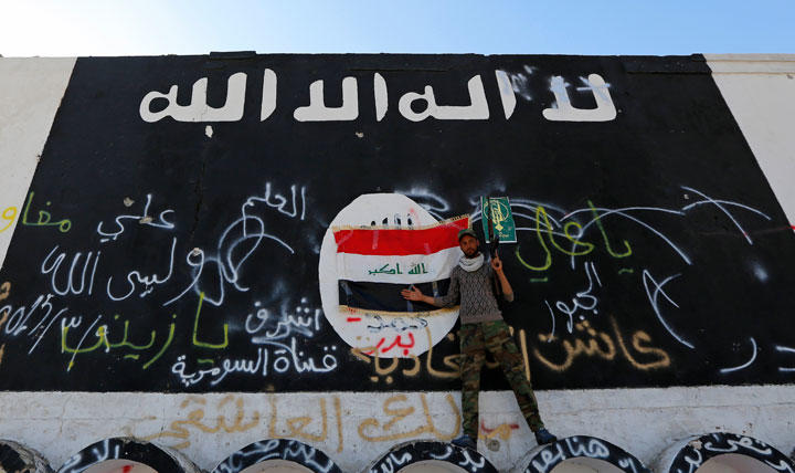 イラクの町アルアラムで壁に描かれたISの旗の前に立つISの民兵（2015年3月）。この後、ISはイラク軍によって町から追い出された　Thaier Al-Sudani -REUTERS