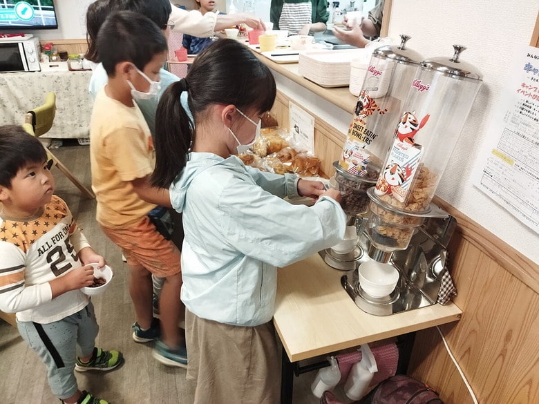 こども食堂のディスペンサーからケロッグのシリアルを取り出す子どもたち
