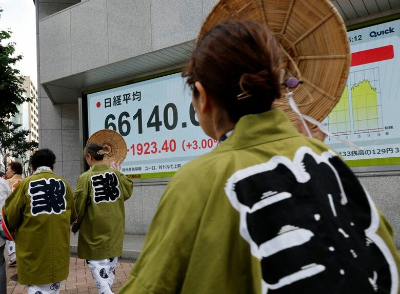 株価ボードの前を通り過ぎる、地元の祭りの参加者。6月12日、都内で撮影。REUTERS/Kim Kyung-Hoon