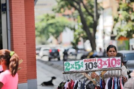 １０月１日、    南米ベネズエラは、ハイパーインフレに対応し、通貨ボリバルからゼロを６つ取り、１００万分の１に切り下げるデノミネーション（通貨単位の切り下げ）を実施した。写真は１日、カラカスの街頭で、米ドル価格で衣料品を売る女性（２０２１年　ロイター/Manaure Quintero）