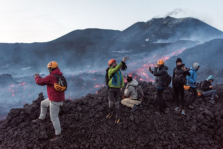 溶岩が燃え盛る噴火口のそばで写真を撮る登山客たち