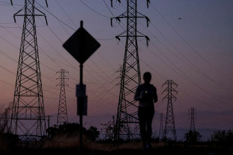 写真は米カリフォルニア州マウンテンビューの送電線と、ジョギングする人影。2022年8月撮影。REUTERS/Carlos Barria