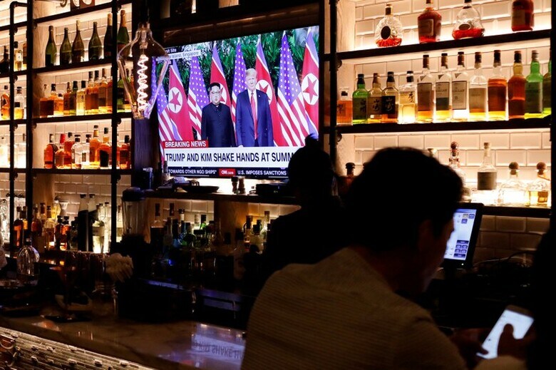６月１３日、ロイター／イプソスの調査によると、トランプ米大統領の北朝鮮問題の対応を支持する人は半数を若干上回った。写真は１１日、米ニューヨーク・マンハッタンのコリアタウンのバーで米朝首脳会談のテレビ中継を見る客の男性ら（２０１８年　ロイター/Andrew Kelly/Files）