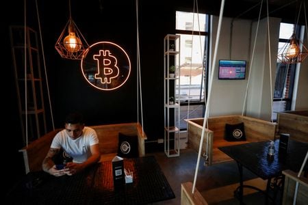 　５月３０日、アルゼンチンの首都ブエノスアイレスの繁華街にあるカフェ「クリプトステーション」では、暗号資産（仮想通貨）相場をリアルタイム表示するスクリーンや「ビットコイン」の巨大なネオンサインに囲まれて、今どきの若者たちがカフェラテやスイーツを注文している。５月５日撮影（２０２２年　ロイター/Agustin Marcarian）