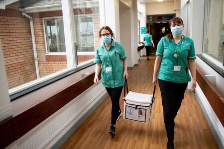 英イングランド公衆衛生局（ＰＨＥ）は２８日、国内の新型コロナウイルスワクチン接種は家庭内感染を最大で半減させるとのデータを公表した。写真はモデルナ製のワクチンが入った冷凍コンテナを運ぶ医療関係者。英ウェールズで７日撮影。（2021年 ロイター/ Jacob King/Pool via REUTERS )