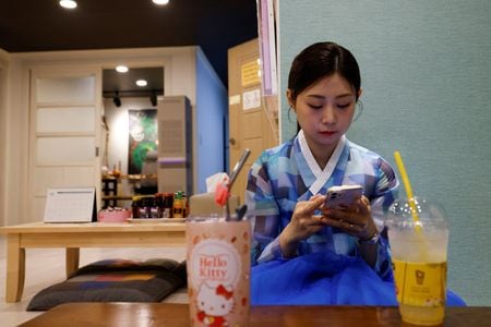 　６月８日、ソウルで活動する巫堂のイ・キョンヒュンさんの祈祷所には、仏像や土着の神々の像とともにロウソクや線香が並べられていた。写真は５月、ソウル市内にある自分の祈祷所でスマートフォンを確認するイさん（２０２４年　ロイター/Kim Soo-hyeon）