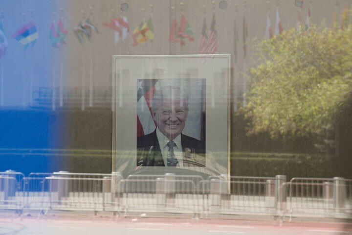 【外交】アメリカ国連代表部の正面に飾られたドナルド・トランプ大統領の肖像写真。通りを挟んで反対側にある国連本部前に掲げられた加盟国の国旗がガラスに映る（本文文末に続く）