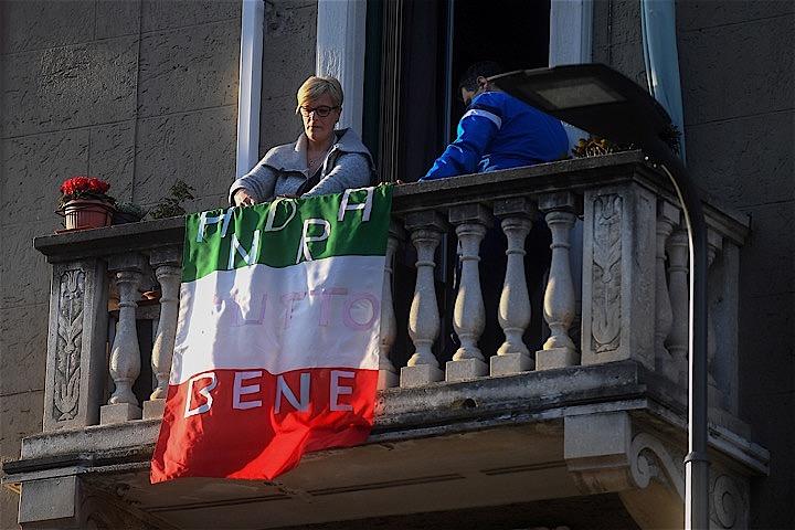 イタリア当局は16日、新型コロナによる国内の死者数が前日から349人増加し2158人になったと明らかにした。写真は16日ミラノ市内で「いつかはよくなる」と手書きしたイタリア国旗を掲げる女性。　Daniele Mascolo - REUTERS
