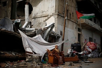 イスラエル軍の砲撃で吹き飛んだ自宅の前に座る女性（ガザ）　Suhaib Salem-REUTERS