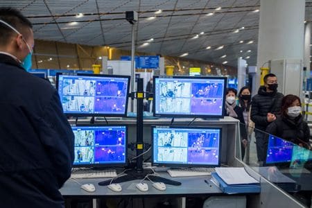 　１０月２０日、中国当局が、新型コロナウイルス防疫対策として定める入国者の隔離期間を１０日間から７日間に短縮することを討議している。写真は北京の空港で到着した人々の体温をモニターする担当者。２０２０年１月撮影（２０２２年　ロイター／Thomas Peter）