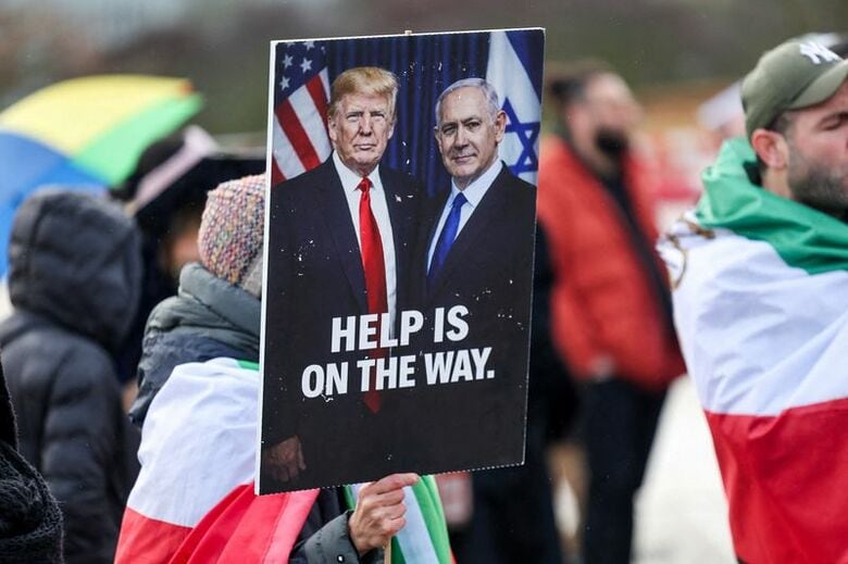 トランプ米大統領とイスラエルのネタニヤフ首相の写真が描かれたプラカードを掲げる人物。2月17日、スイスのジュネーブで撮影。REUTERS/Pierre Albouy