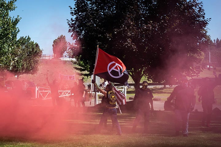 衝突の後、アンティファの旗を奪って掲げるプラウド・ボーイズのメンバー（6月18日、オレゴン州オレゴンシティー。赤い煙は武器に使われた熊よけスプレー））　REUTERS/Maranie Staab