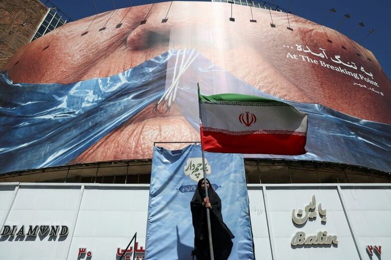 トランプ米大統領とホルムズ海峡を描いた反米看板の近くで、イラン国旗を掲げる女性。5月25日、テヘランで撮影。WANA提供写真。REUTERS