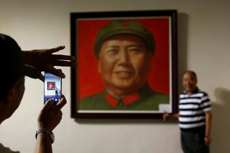 ９月８日、中国共産党の内外を問わず、過去３０年間の市場主義改革は行き過ぎであり、貧困などの社会格差や汚職を生んでいると考える左派（保守派）勢力にとって、９日に没後４０年を迎える毛沢東主席は有力なシンボルとなっている。写真は同主席の肖像画の隣でポーズをとる男性。北京での毛沢東関連の美術展示会にて（２０１６年　ロイター/Thomas Peter）