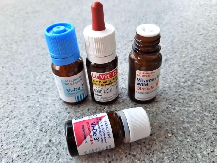 小瓶に入った液状ビタミンD(D3)の例。1滴のD含有量(濃度)は様々で左より100IU、400IU、500IU（IUは生体に対する効力で表す単位）。必要に応じて1回数滴服用する。手前は1か月分の目安量を1回で取るもので、全容量５mlをコップの水に混ぜて飲む（撮影筆者）