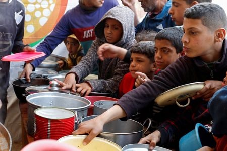 　４月１日、国連は、パレスチナ自治区ガザで世界食糧計画（ＷＦＰ）が支援するパン店２５軒全てが物資不足から営業を停止したにもかかわらず、イスラエルがガザには長期にわたり十分な食料があると主張したことは「馬鹿げている」と非難した。写真は、食事を待つパレスチナの子どもら。３月９日、ガザ南部のハンユニスで撮影（２０２５年　ロイター/Hatem Khaled）