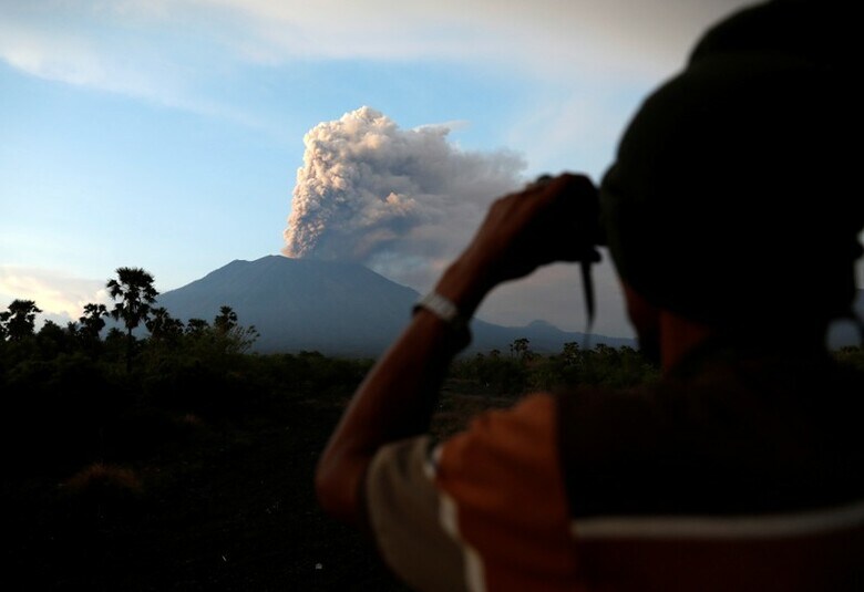 １１月２８日、インドネシア運輸省は、バリ島のアグン山噴火による火山灰の影響で、同島のイ・グスティ・ングラ・ライ国際空港の閉鎖を現地時間２９日午前７時まで２４時間延長すると明らかにした。噴煙の上がるアグン山を見る地元住民。バリ島で撮影（２０１７年　ロイター／Darren Whiteside）