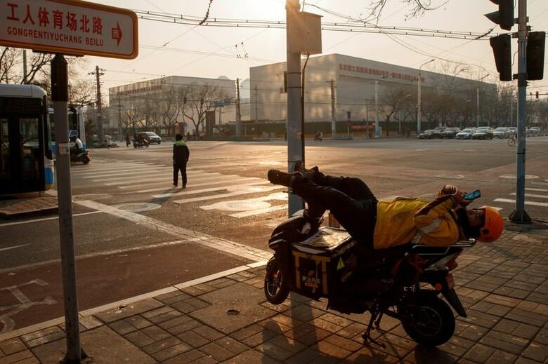 写真は電動自転車の上で休憩する配達員。2020年1月、北京で撮影。REUTERS/Thomas Peter
