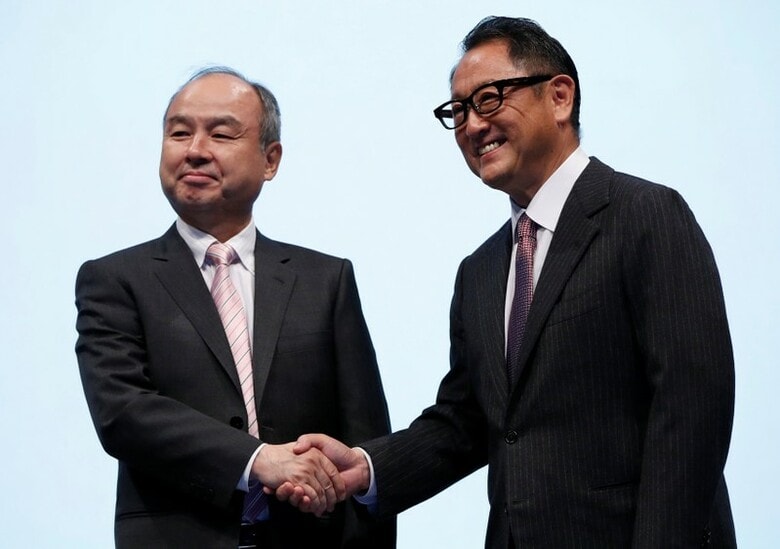 １０月４日、トヨタ自動車とソフトバンクの２大企業が、モビリティサービスの構築に向けて初めて本格的に手を組んだ。写真は都内の記者会見場で握手を交わすトヨタの豊田章男社長（右）とソフトバンクグループの孫正義社長（２０１８年　ロイター/Issei Kato）
