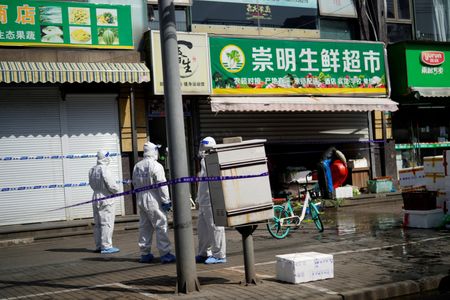 　３月２９日、中国で人口が最多の上海市は、新型コロナウイルスの感染拡大を受けて前日から開始したロックダウン（都市封鎖）措置をさらに強化し、一部の住民に検査以外の目的での外出を禁止した。写真は封鎖された食料品店の外に立つ防護服の警官たち。上海で撮影（２０２２年　ロイター／Aly Song）