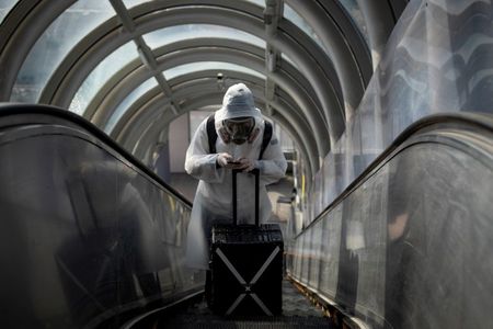 中国では２２日、新たに４６人の新型コロナウイルス感染者が報告された。国家衛生健康委員会によると、このうち４５人が海外からの入国者で、新規感染者は４日連続で前日を上回った。写真は防護服で全身を包んだ旅行者。３月２０日、北京の鉄道駅で撮影（２０２０年　ロイター/Thomas Peter）