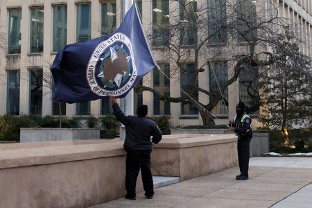 　今年３月、米連邦政府の人事管理局（ＯＰＭ）が幹部らの運転手を雇う計画がメディアに報じられると、政府関係者はすぐにリーク元を探し出すための調査を開始した。写真は米首都ワシントンのＯＰＭ本部前で旗を片付けるスタッフ。２月１３日撮影（２０２５年　ロイター/Tierney L. Cross）