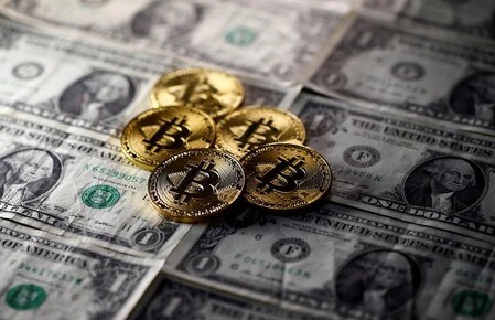 　１２月６日、仮想通貨ビットコイン相場は、節目の１万２０００ドルを突破し過去最高値を更新。仮想通貨の実質的な価値に対する懐疑的な見方やバブルに対する警戒感があるにもかかわらず、上値指向を強めている。写真は米ドル札とビットコインのレプリカ（２０１７年　ロイター／Dado Ruvic）