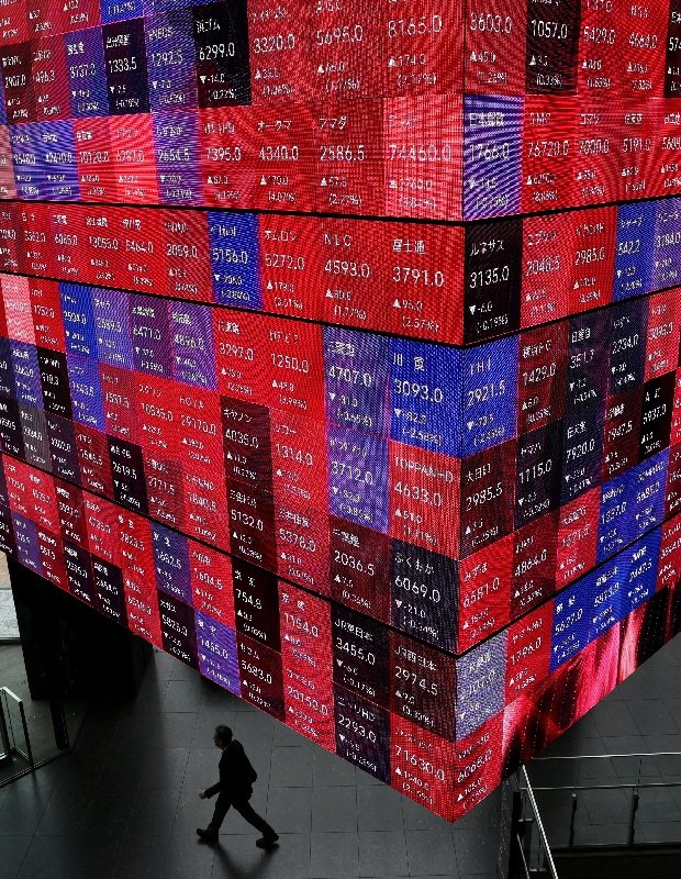 株価を表示するスクリーンの付近を歩く男性。東京都内で4月撮影。REUTERS/Issei Kato