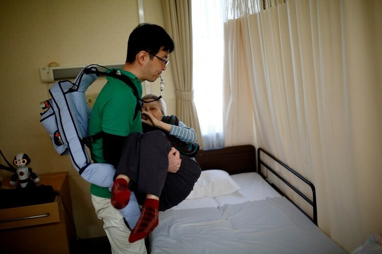 ３月３０日、日本の介護現場には現在、最先端のロボットが続々と登場し、様々な介護ニーズに応えている。写真は「マッスルスーツ」を着て入居者を持ち上げる介護職員。2月に東京の老人ホームで撮影（2018年　ロイター／Kim Kyung Hoon）